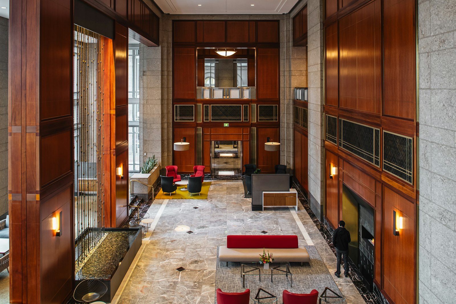 Grand building lobby with rich mahogany-toned wood paneling, marble floors and warm sconce lighting
