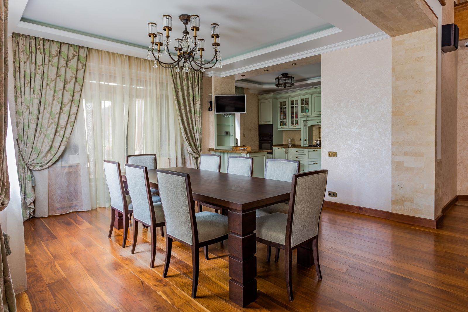 Dark walnut dining table with eight upholstered chairs in an elegant dining room with wood floors and a chandelier.