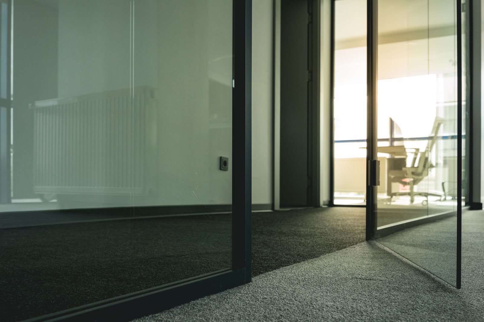 Low sun blasting through black-framed glass office doors, washing out a window-side desk and monitor