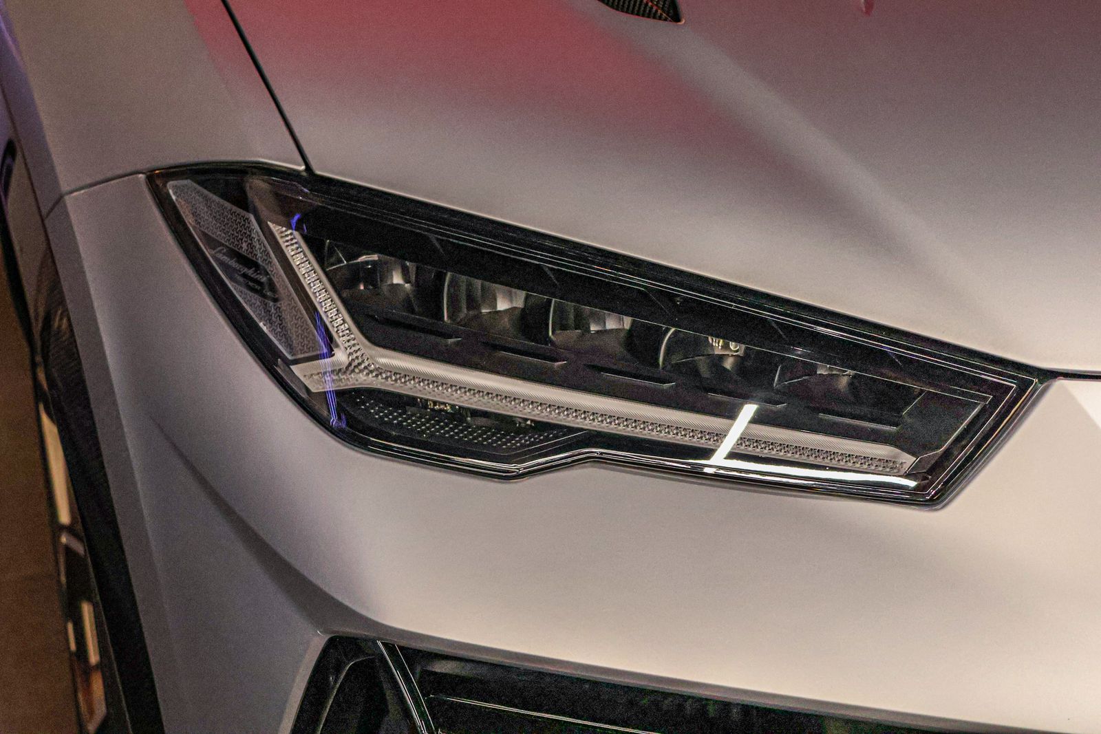 Close-up of a Lamborghini Urus LED headlight with a crystal-clear lens on a satin-silver front end.