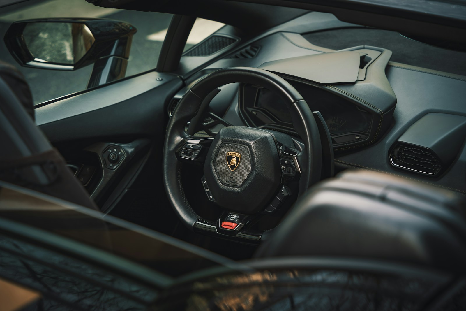 Driver's view of a dark Lamborghini cabin with stitched leather dashboard, console trim and steering wheel
