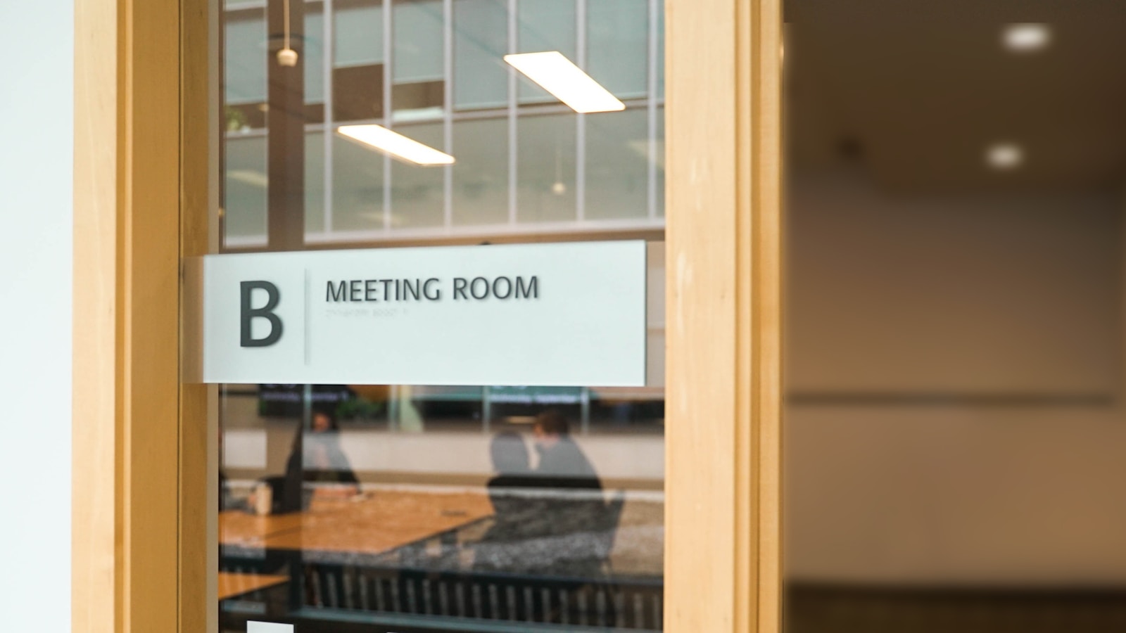 Room-name signage applied to the glass front of a modern office meeting room