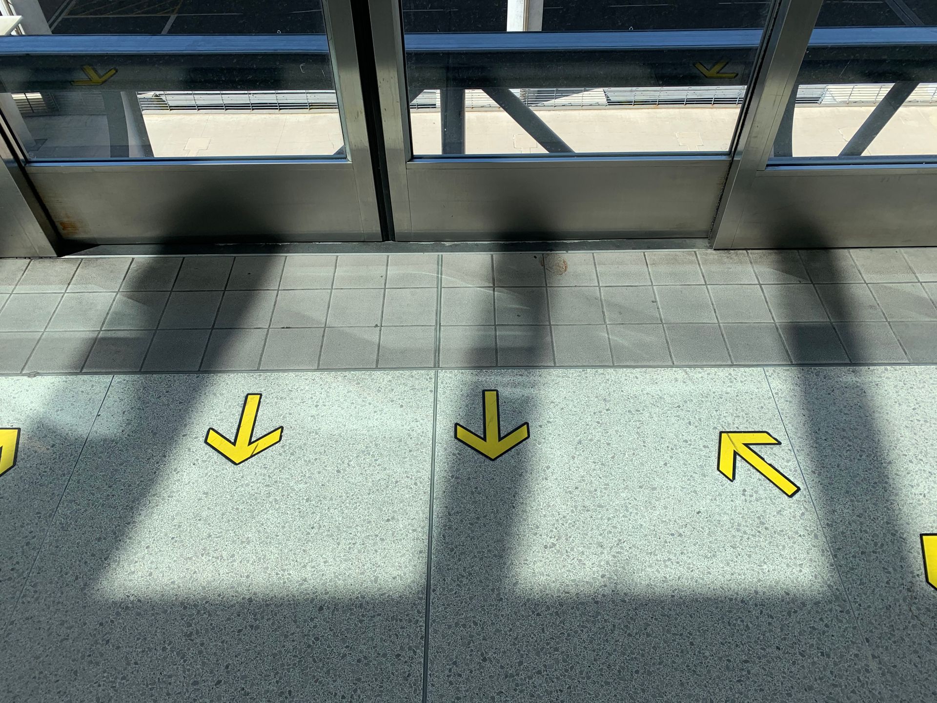 Yellow directional arrow decals applied to a tiled interior floor beside glass entrance doors
