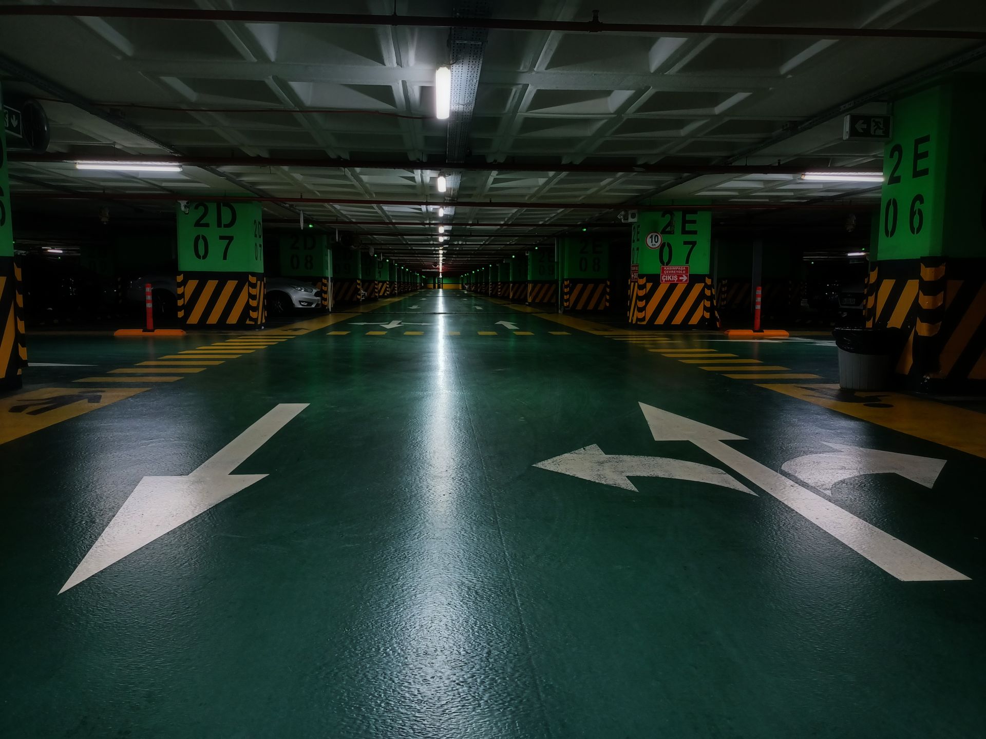 White directional arrows and yellow-black hazard striping marking lanes on a green parking-garage floor