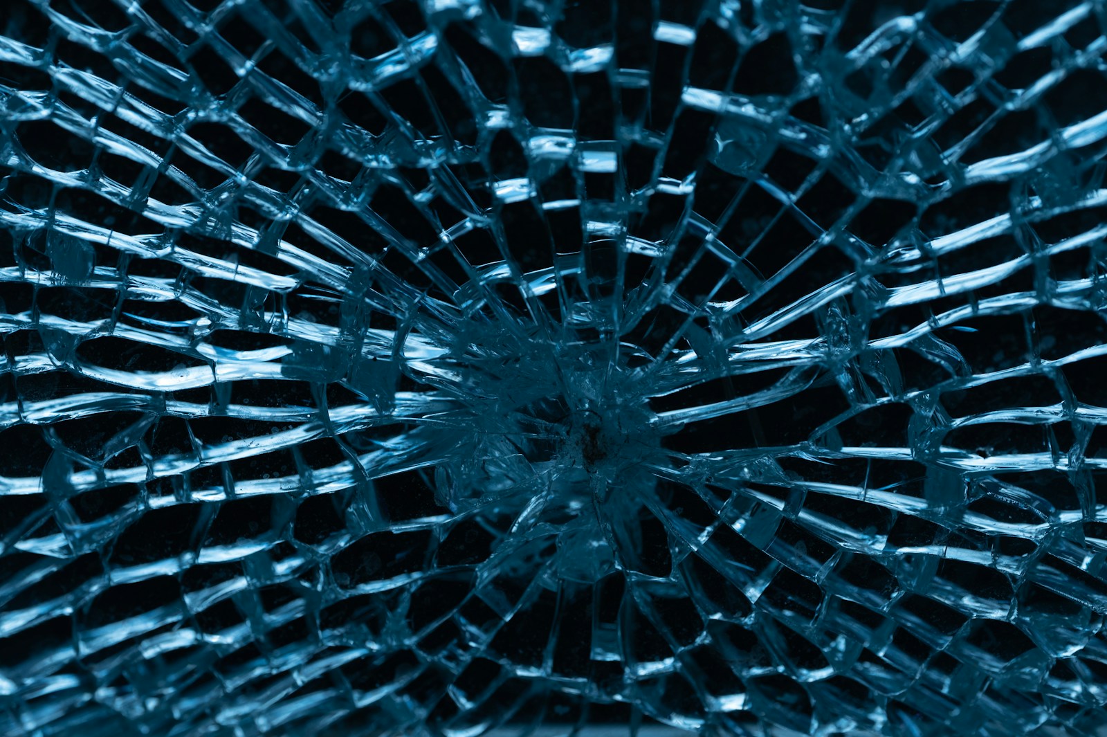 Shattered glass pane with a dense spiderweb crack pattern still holding together in one sheet
