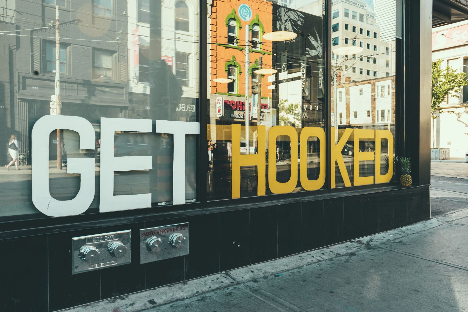 Storefront glass with large white and yellow 'GET HOOKED' lettering graphics, street reflections visible in the window