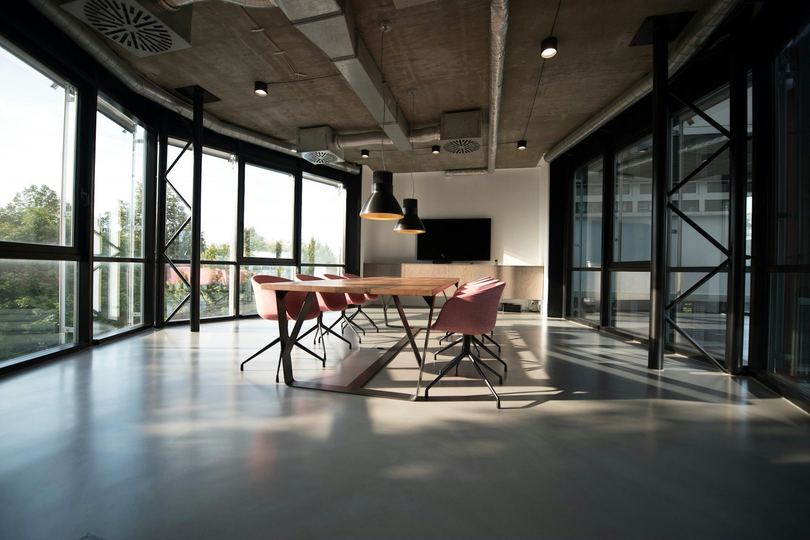 Hard sunlight pouring through floor-to-ceiling glass walls onto the floor of a modern loft meeting room