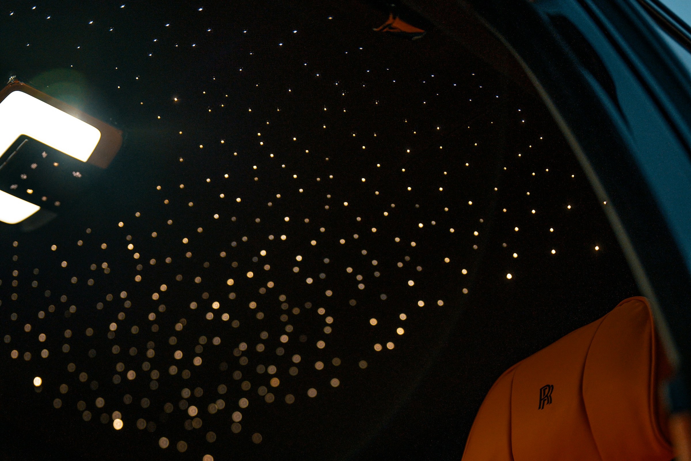 Fiber-optic starlight headliner glowing above orange leather seats in a Rolls-Royce cabin