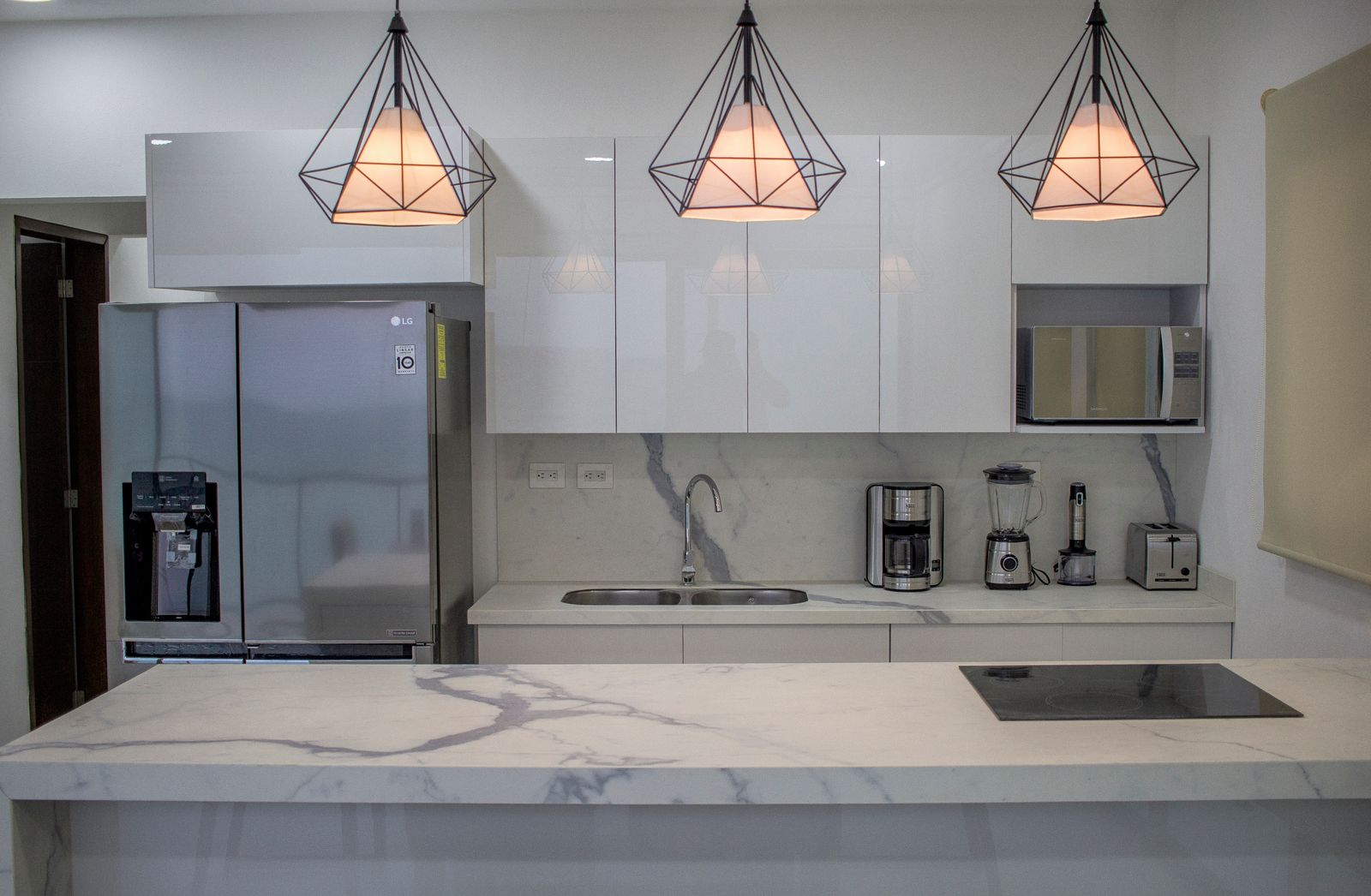 White marble island and matching marble backsplash in a modern kitchen under geometric pendant lights.