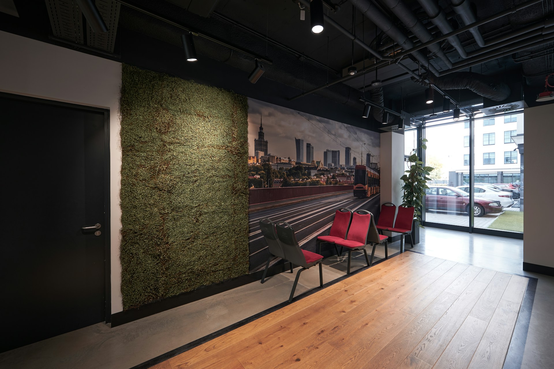 Printed city-skyline wall mural spanning a modern office waiting area with a moss accent wall and seating