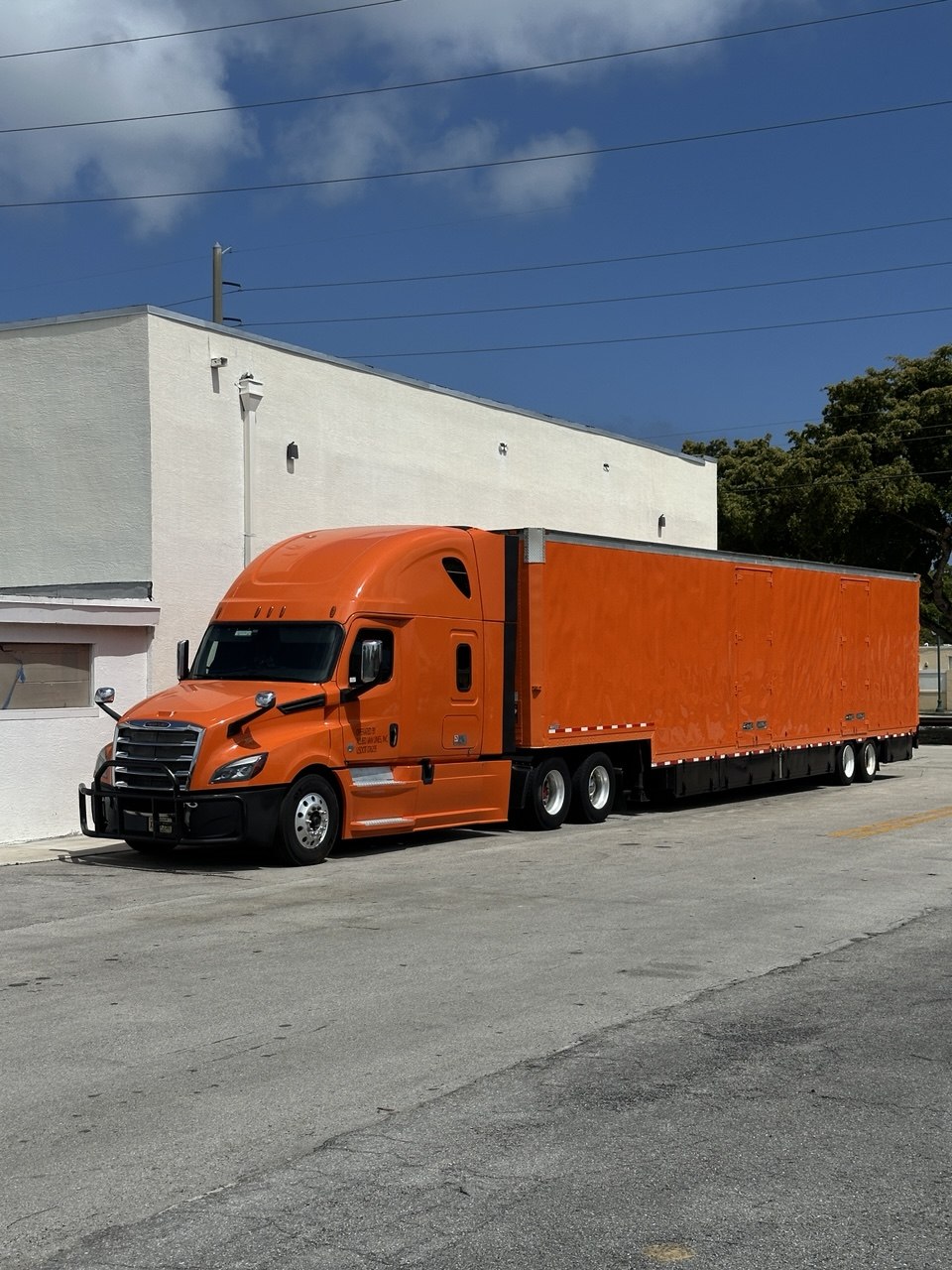 Semi truck and 53-foot trailer wrapped in high-gloss orange vinyl outside the Wrap Trap shop